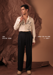 Man wearing HORD Upside Down ivory shirt with black beaded cursive script and arrow, full-length studio shot