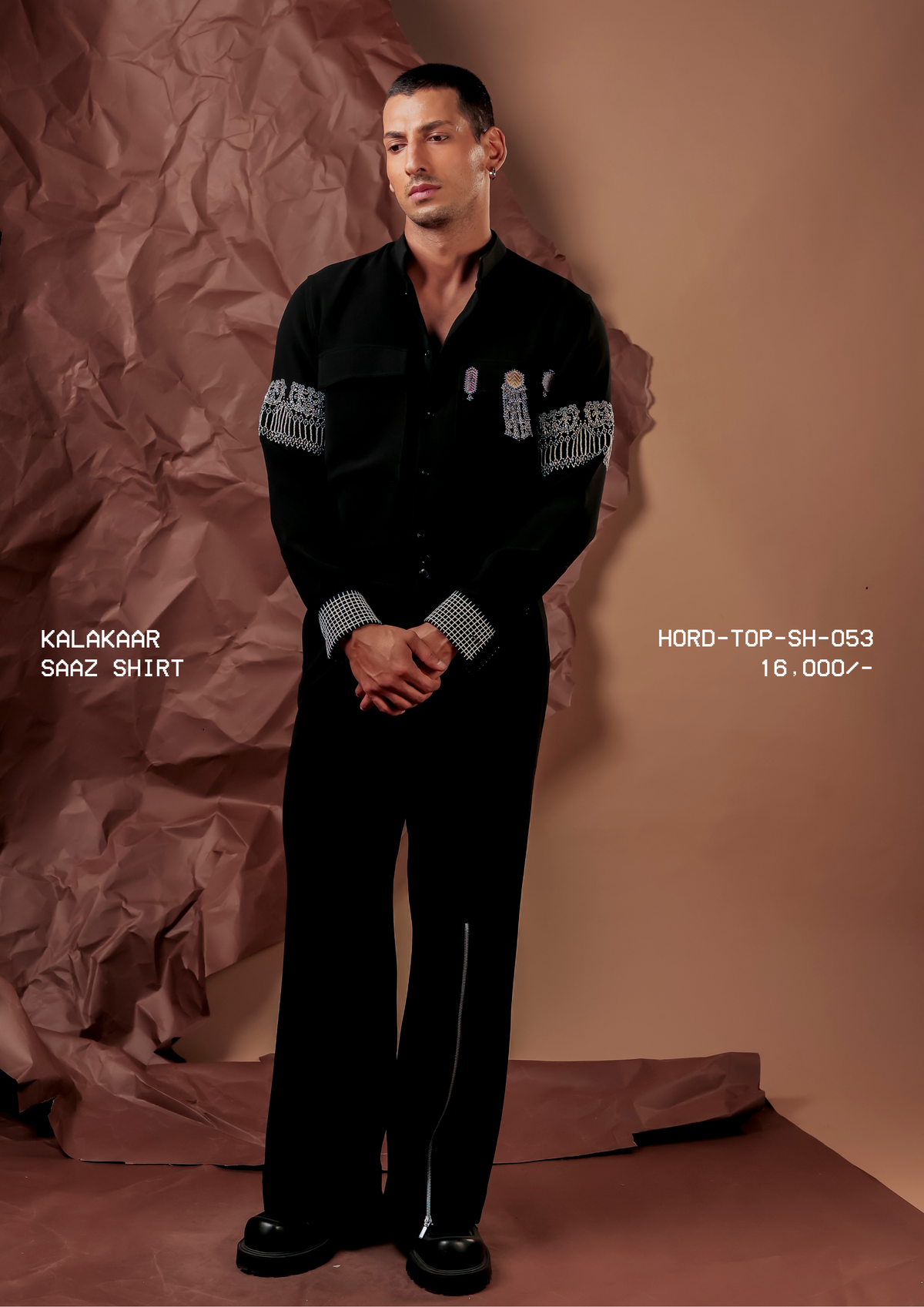 Man wearing HORD Saaz Shirt black shirt with silver fringed armbands and houndstooth cuffs, full-length studio shot