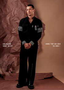Man wearing HORD Saaz Shirt black shirt with silver fringed armbands and houndstooth cuffs, full-length studio shot