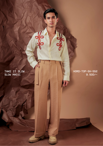 Man wearing HORD Slow Magic butter cream shirt with red cord-knot appliques on the shoulders, styled with tan trousers