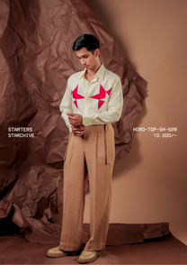 Man wearing HORD Starchive butter cream shirt with two hot pink star appliques on the chest, styled with tan trousers