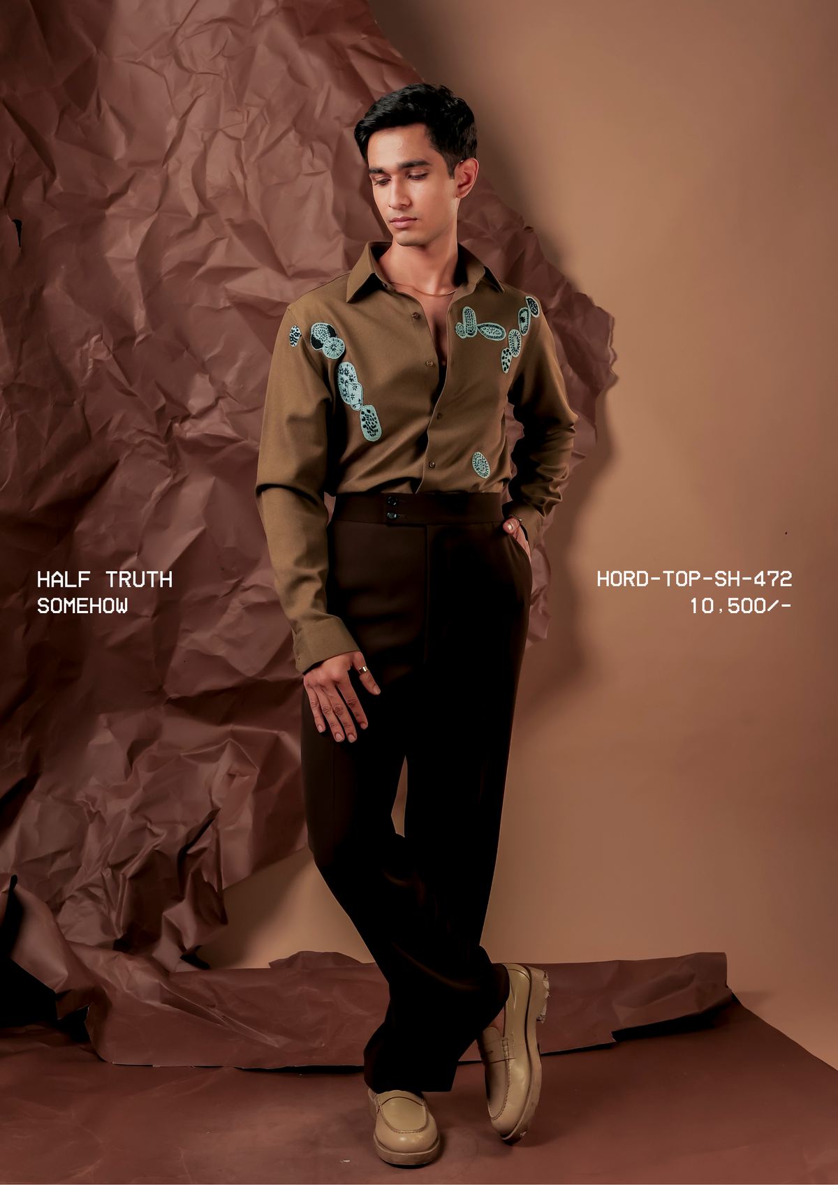 Man wearing HORD Somehow olive brown shirt with aqua embroidered paisley motifs, full-length studio shot