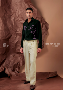 Man wearing HORD One Of 1 dark green shirt with lilac beaded cursive script, styled with pale pleated trousers