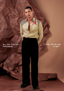 Man wearing HORD Hypotenuse beige shirt with black and white geometric shoulder panels and red monogram, full-length studio shot