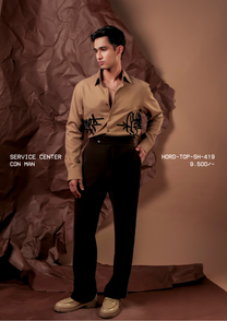 Man wearing HORD Con Man camel shirt with black graffiti tag embroidery at the waist, full-length studio shot