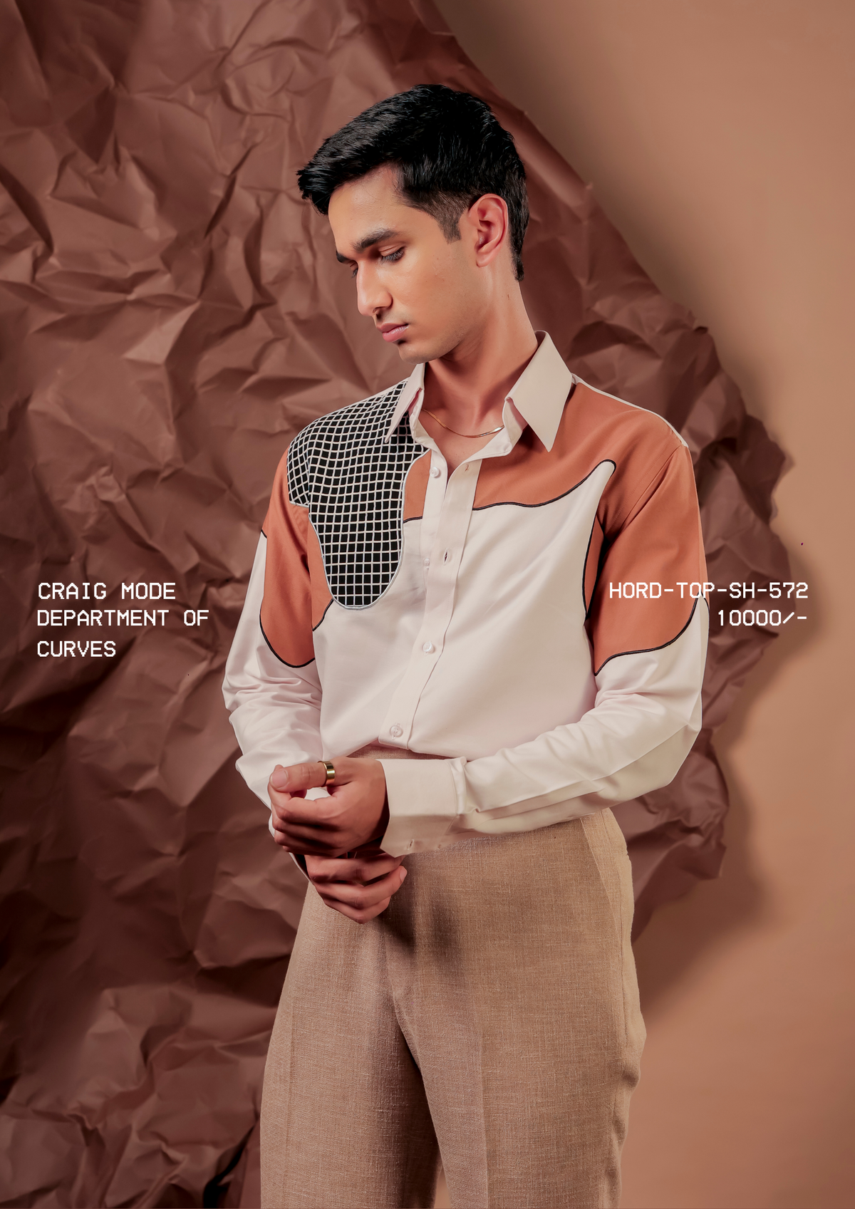 Man wearing HORD Department of Curves off-white shirt with rust shoulder panels and black grid yoke, styled with beige trousers