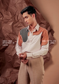 Man wearing HORD Department of Curves off-white shirt with rust shoulder panels and black grid yoke, styled with beige trousers