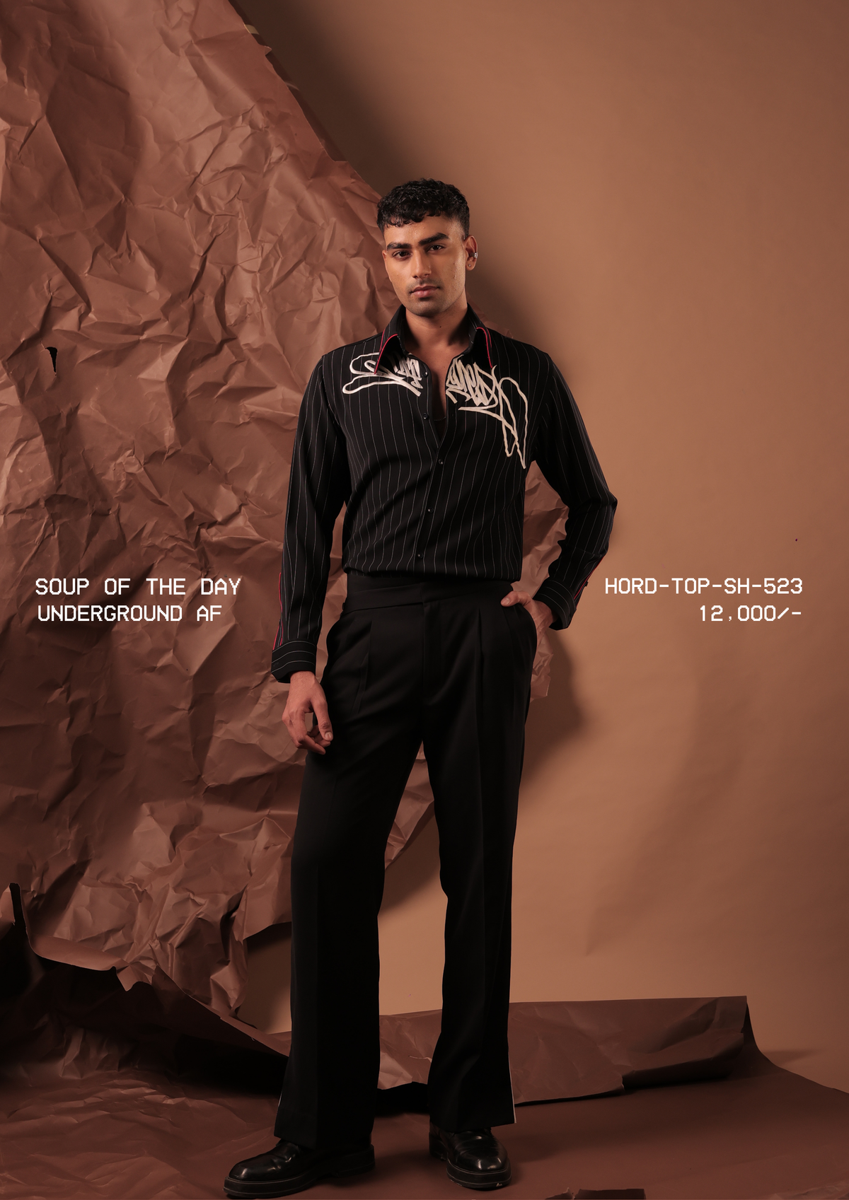 Man wearing HORD Underground AF black pinstripe shirt with ivory graffiti embroidery, full-length studio shot