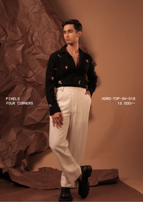 Man wearing HORD Four Corners black shirt with scattered multicolour pixel embroidery, styled with cream trousers